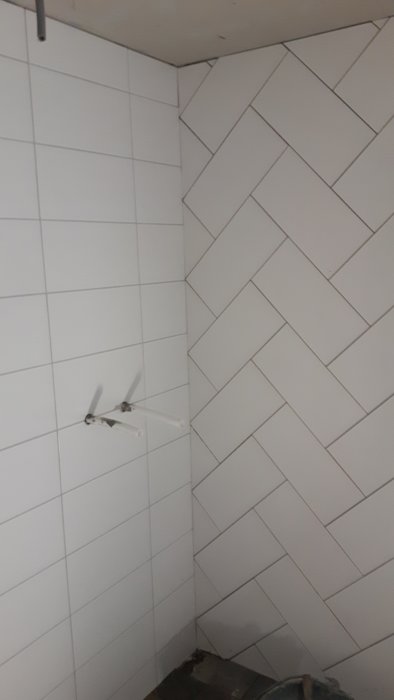 Kaklade väggar med fog i vitton och synliga rörstumpar i renoverat badrum.