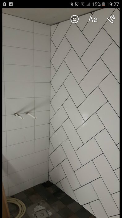 Kakel i fiskbensmönster i antracit och vita väggar i en byggmiljö, med omärkt golvyta och kablar.