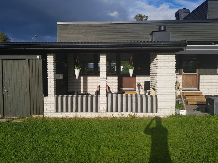 Uteplats med vit putsad tegelvägg och tre pelare, varav en inte når upp till taket, samt diskussionspunkt för renovering.