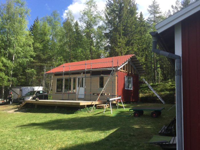 Hus med nytt rött tak och byggnadsställning under en klar himmel, omgivet av grönska.