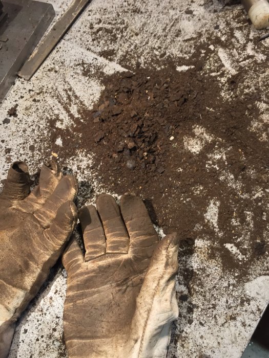 Arbetsbänk med ett par använda handskar och rester av patina från ett renoverat skruvstäd.