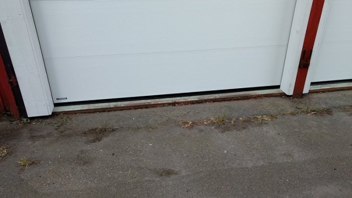 Nya vita garageportar med synlig metallkant vid marken som behöver åtgärder för att hindra regnvatten.