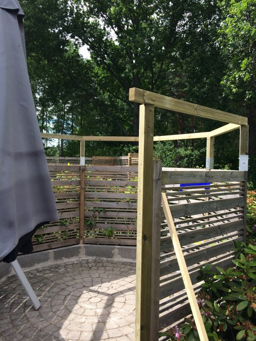 Renoverad uteplats med nytt trästaket och stolpar mot en bakgrund av gröna träd och buskar.