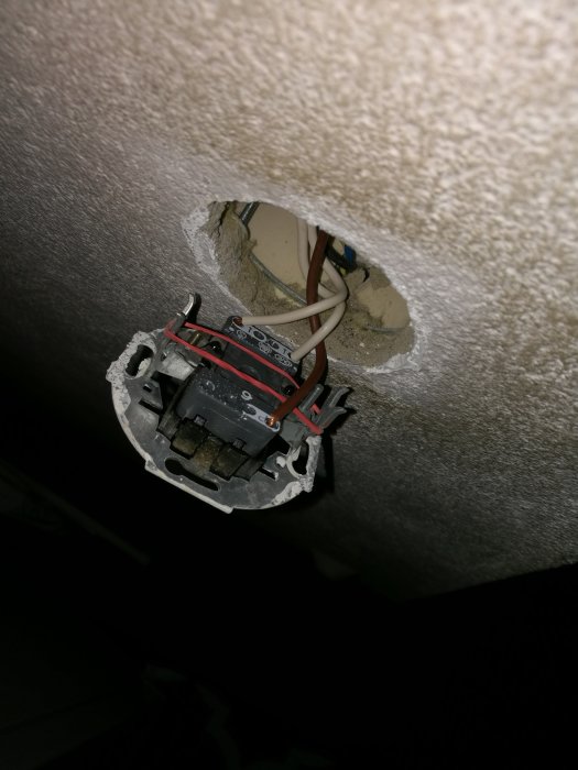 Eluttag som är delvis urtaget ur väggen med synliga kablar och installationsdetaljer.