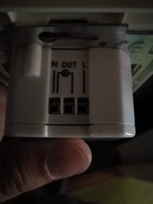 Hand håller en elektrisk installationsenhet med tydliga märkningar för N, OUT och L, redo för att kopplas.