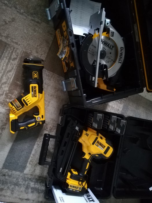 Dewalt-verktyg med cirkelsåg och spikpistol i öppna svarta förvaringslådor på ett grått golv.