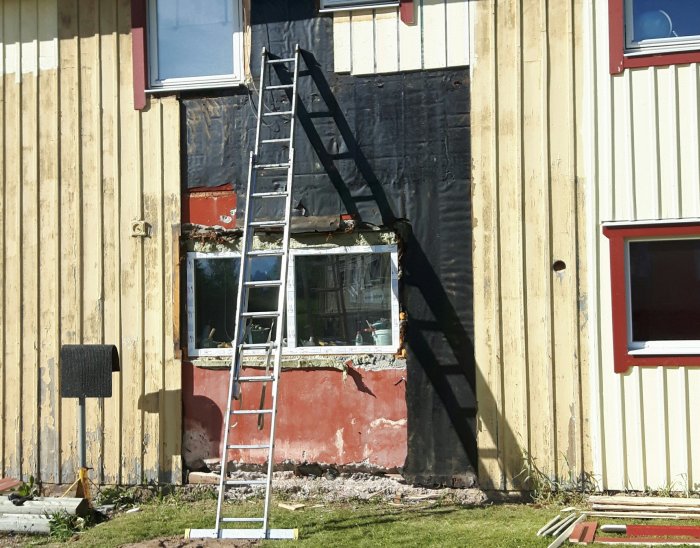 En stege lutad mot en oavslutad yttervägg med isolering synlig där panel ska bytas.