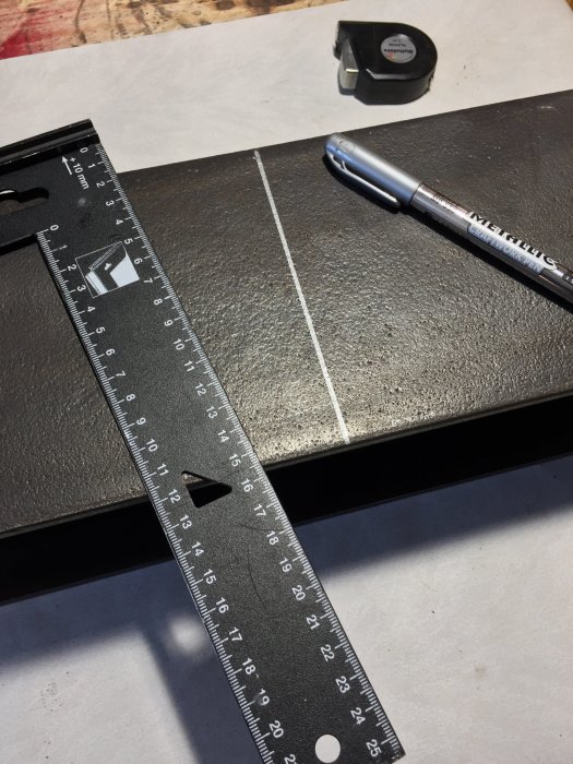 Metallstativ med utmätta borrningslinjer, T-square, mättpenna och måttband på arbetsbänk.