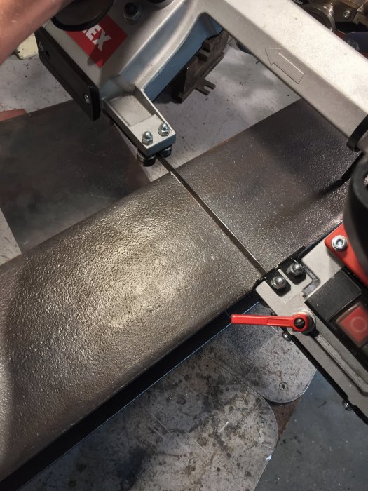 Metallstativ i en bandsåg under kapning, smörjmedel syns på ytan för bättre borrning och gängning.