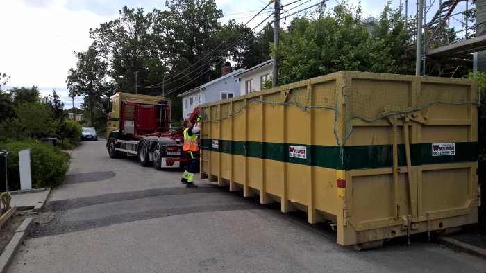 Lastbil hämtar en stor gul container från Wiklunds Åkeri på en bostadsgata.