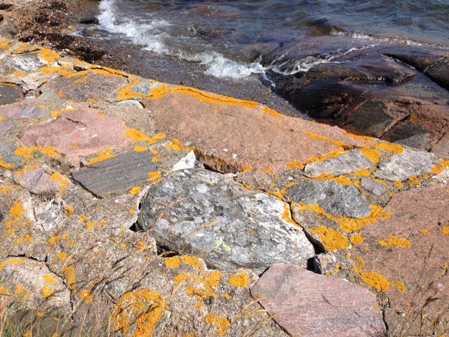 Erosionspåverkad naturstensgång längs kusten med synliga underlagsgap och saltvatten i bakgrunden.