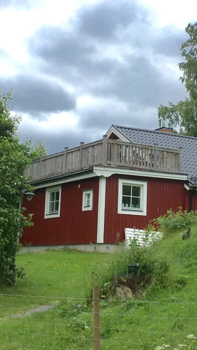 Rött hus med en oanvänd takterrass med staket ovanpå, under en molnig himmel.