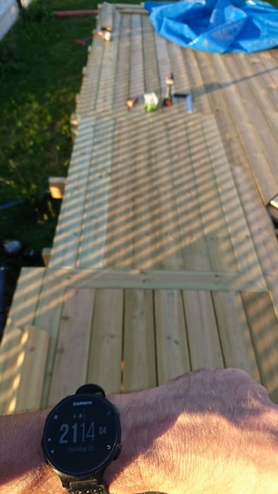 Nytrallat däck i kvällsljus med verktyg och flaska synliga, förgrundens armbandsur visar tiden 21:14.