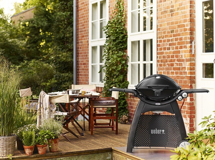 Altan med möbler och en Weber Q 3200 gasolgrill framför tegelhus med klätterväxt.