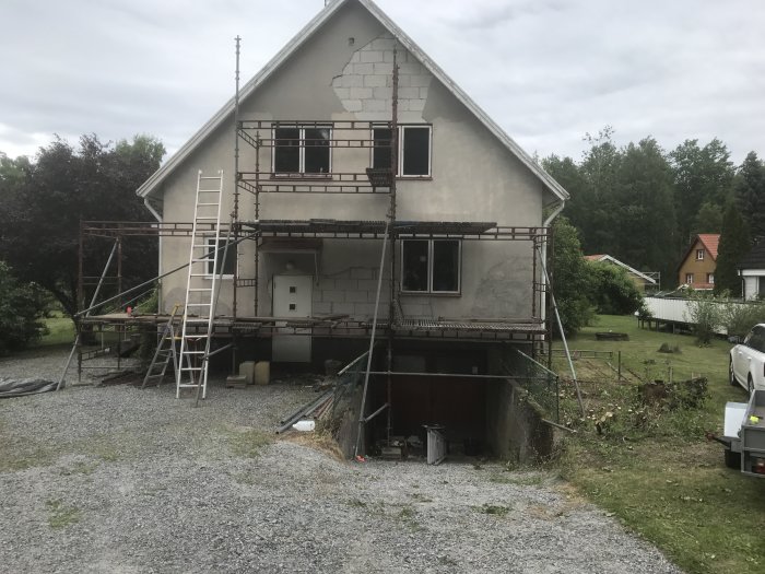 Hus med uppsatt byggnadsställning inför renovering, sliten puts och ett påbörjat fönsterbyte.