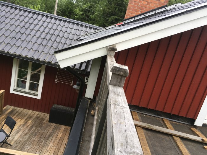 Del av hus med svart takpannor och röda träväggar samt en träaltan under konstruktion.