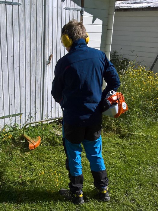 Person i arbetskläder använder en bensindriven röjsåg för att trimma gräs.