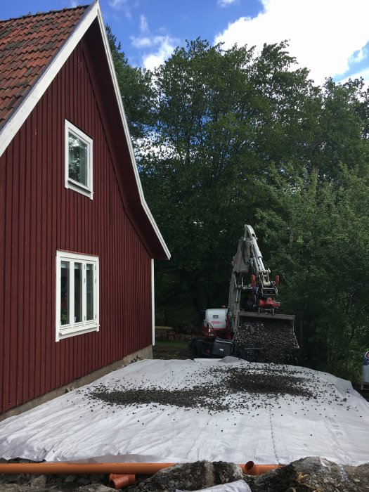 Röd huskropp med nytt dagvatten och grundarbete, lastbil tippar makadam.