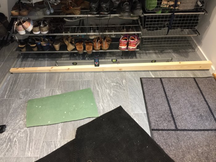 Installation av skjutdörrsskena på golvet med vattenpass, omgiven av skor och ett grönt knäskydd.