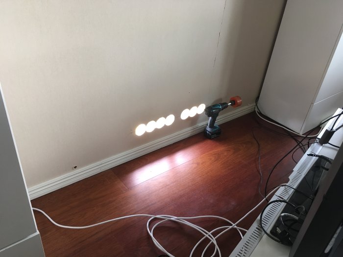 Installation av nio vägguttag och kablar på trägolv vid en vägg, borrmaskin till höger.