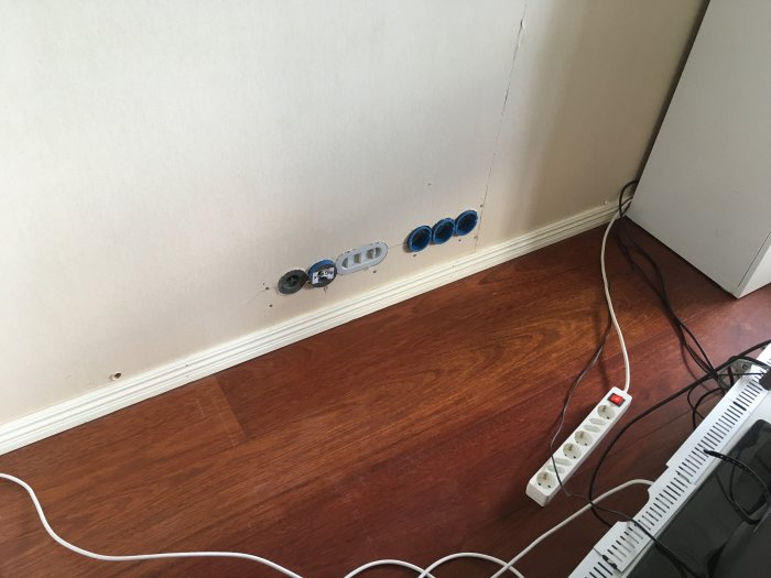 Nyinstallation av nio eluttag, två datauttag och antennuttag i en vägg nära golvet med lösa kablar och grenkontakt.