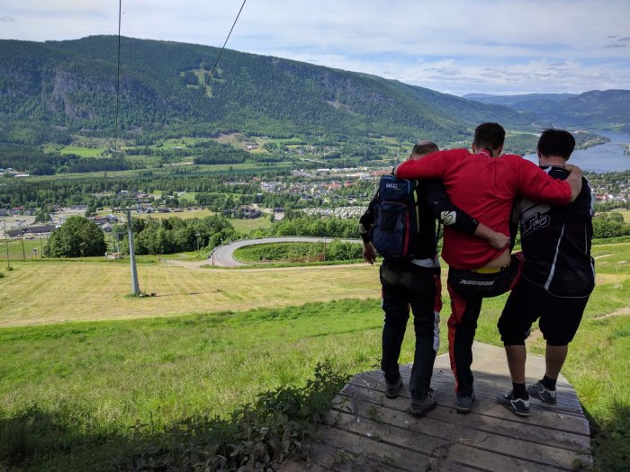 Tre vänner står arm i arm och tittar på utsikten över en dal och sjö från en bergstopp.