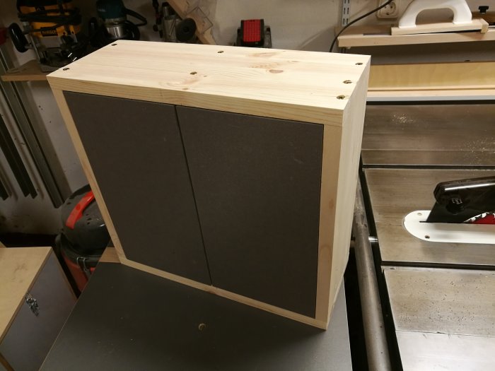 Prototyp av en skänk i trä med tre högerhängda, innanförliggande dörrar och synliga gångjärn, på en arbetsbänk.