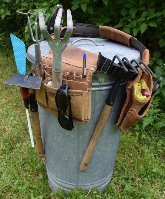 Ett verktygsbälte med trädgårdsverktyg hängande på en kompostbehållare utomhus.