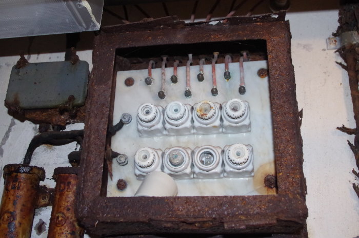 Gammal elcentral med marmorplatta, rostig metallram och porslinssäkringar.