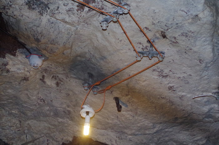 Gammaldags elinstallation med kabeldragningar i porslinshylsor och lampa i taket av bergsrum.