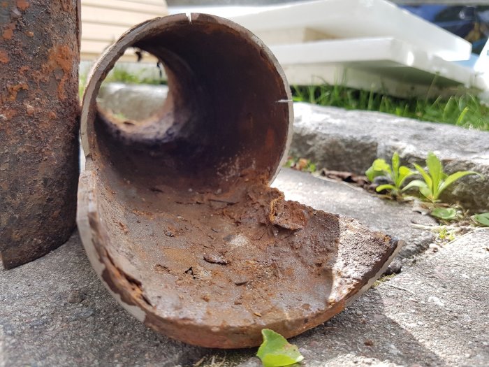 Närbild på en kraftigt korroderad gjutjärnsavloppsrörsektion med tunna väggar.