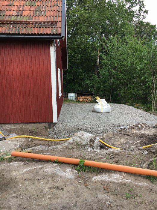 Nyanlagt dagvattensystem med orangea rör vid ett hus omgivet av grus och grönska.