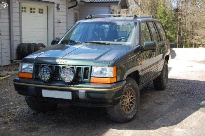 Grön Jeep Grand Cherokee parkerad framför garage, till salu för byggtransporter.