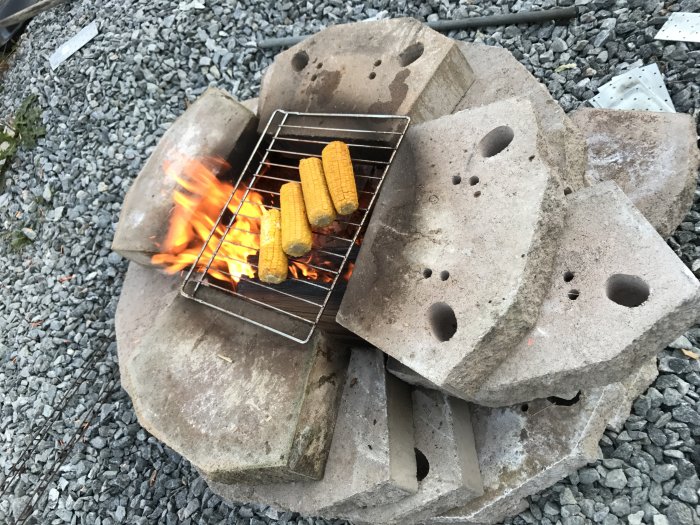 Hemmagjord temporär grill byggd av betongblock med grillade majskolvar över öppen eld.