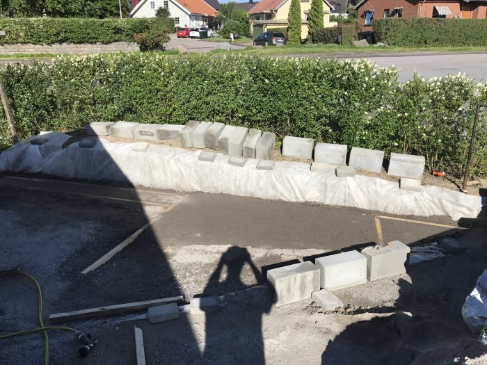 Halvbyggd mur av betongblock med verktyg och byggmaterial framför, tidigt skede av projektet.