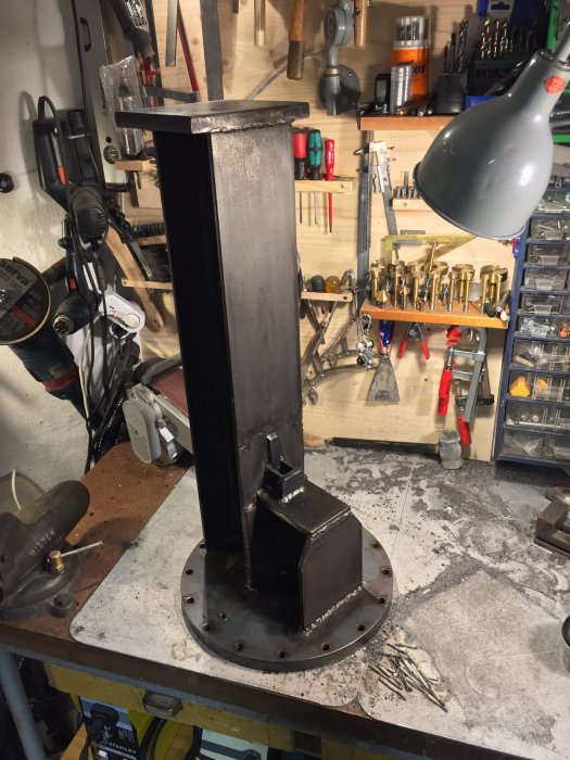 Hemmagjord pelare i metall på verkstadsbänk, väger ca 80-90 kg och ser robust ut.