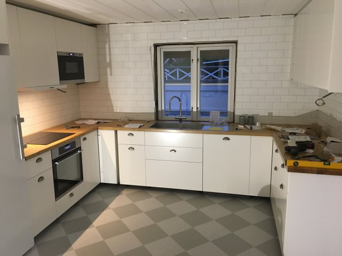 Kök under renovering med installerad diskmaskin, vita skåp och träbänkskiva, verktyg på ytan.
