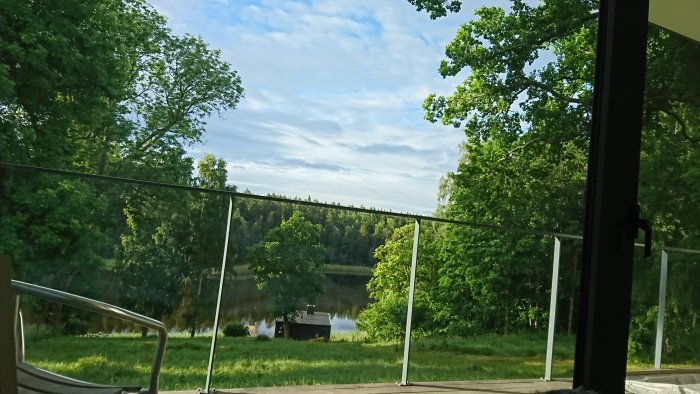 Utsikt från ett sovrumsfönster med sommarmoln, träd och en liten sjö, tagen på morgonen.