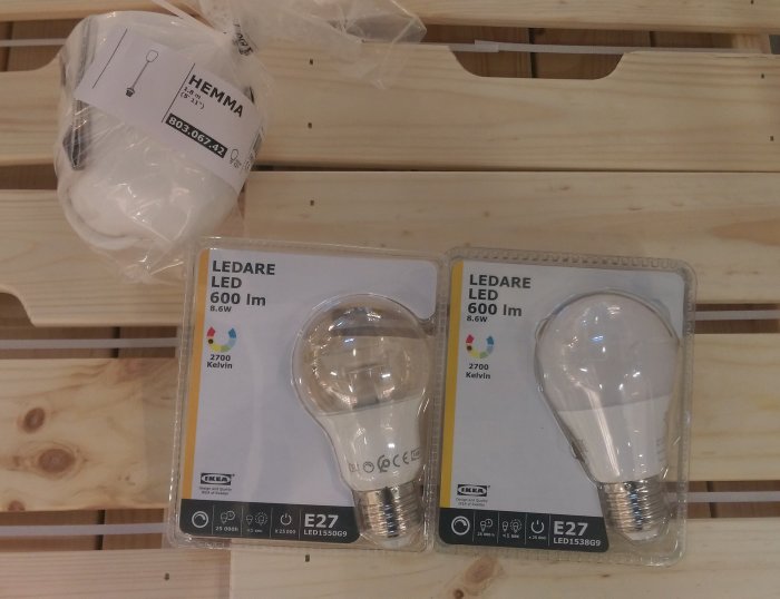 Två LEDARE LED-glödlampor från IKEA med E27-sockel, en klar och en opalvit, bredvid en lampupphäng.