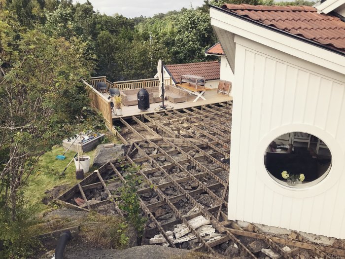 Vy över ett pågående altanbygge, delvis demonterad gammal trall och en nykonstruerad altandel bredvid en byggnad.