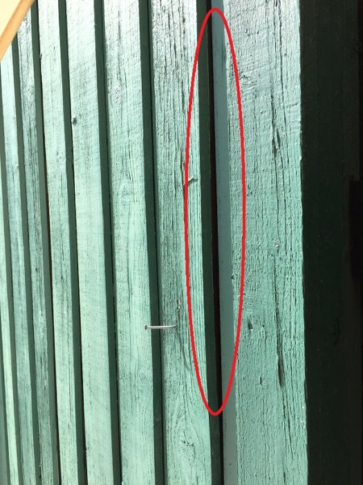 Öppning mellan träpaneler på fasad markerad med röd cirkel.