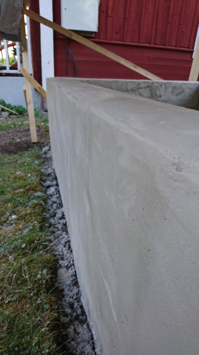 Hörn av nyligen putsad odlingsbädd av lecablock utomhus intill röd stuga.