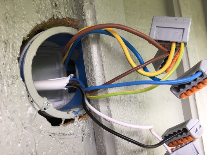 Öppen elektrisk dosa i vägg med flera färgade kablar och kopplingsklämmor för markisens installation.