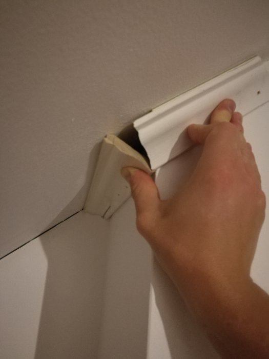 Hand som håller två trälistbitar i ett hörn där den ena biten inte passar helt korrekt.