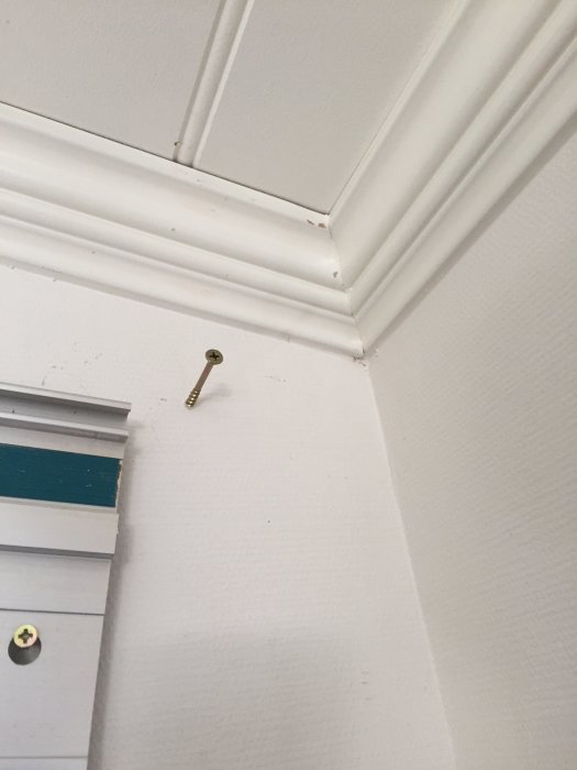 Vitmålat förkroppat innertakshörn där en kort och en lång list möts i en snedtaksvinkel över en skruv.