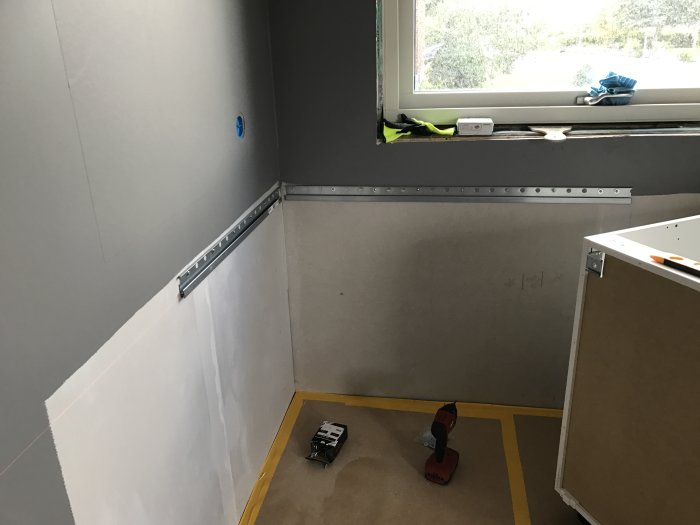 Hörn av ett kök under renovering med en oskylld IKEA upphängningsskena och köksskåpsstomme på golvet.