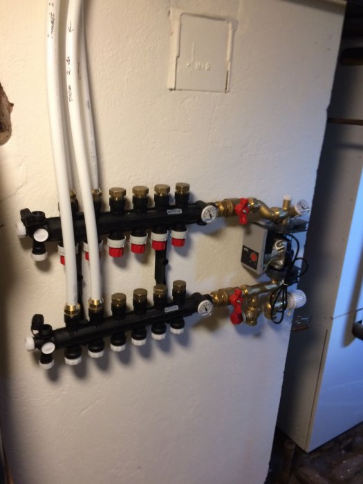 Golvvärmefördelare med shunt monterad uppochner på vägg med utstickande vita rör.