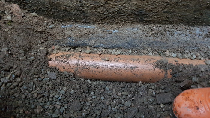 Grävd jord som exponerar dräneringsrör, indikerar högt liggande rör jämfört med omgivande mark.
