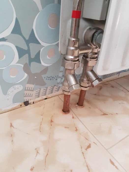 Radiator med kopplade rör och ventiler som läcker vid anslutningen med golvet i bakgrunden.