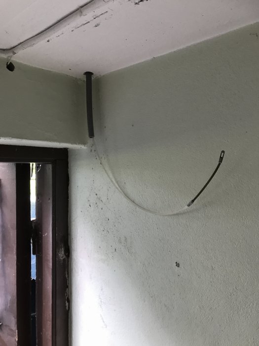 Ofullständig installation av elkabel på en betongvägg intill ett fönster.